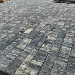 Krystian Marcik - Ułożona nawierzchnia z prostokątnej kostki w odcieniach szarości i bieli, z widocznym fragmentem przygotowanego wykopu pod kolejne elementy.