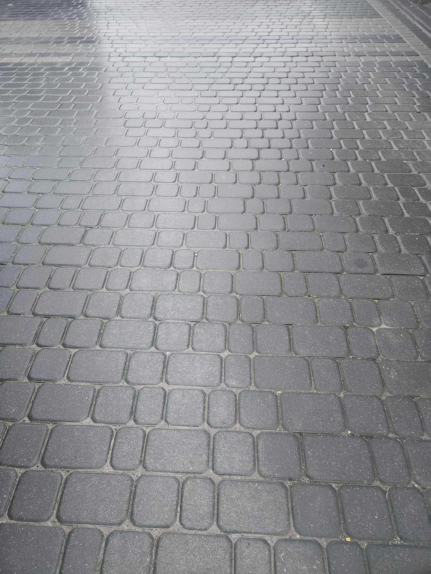 Powierzchnia wyłożona szarą, prostokątną kostką brukową ułożoną w regularny wzór, widok z góry pod kątem, ukazujący perspektywę