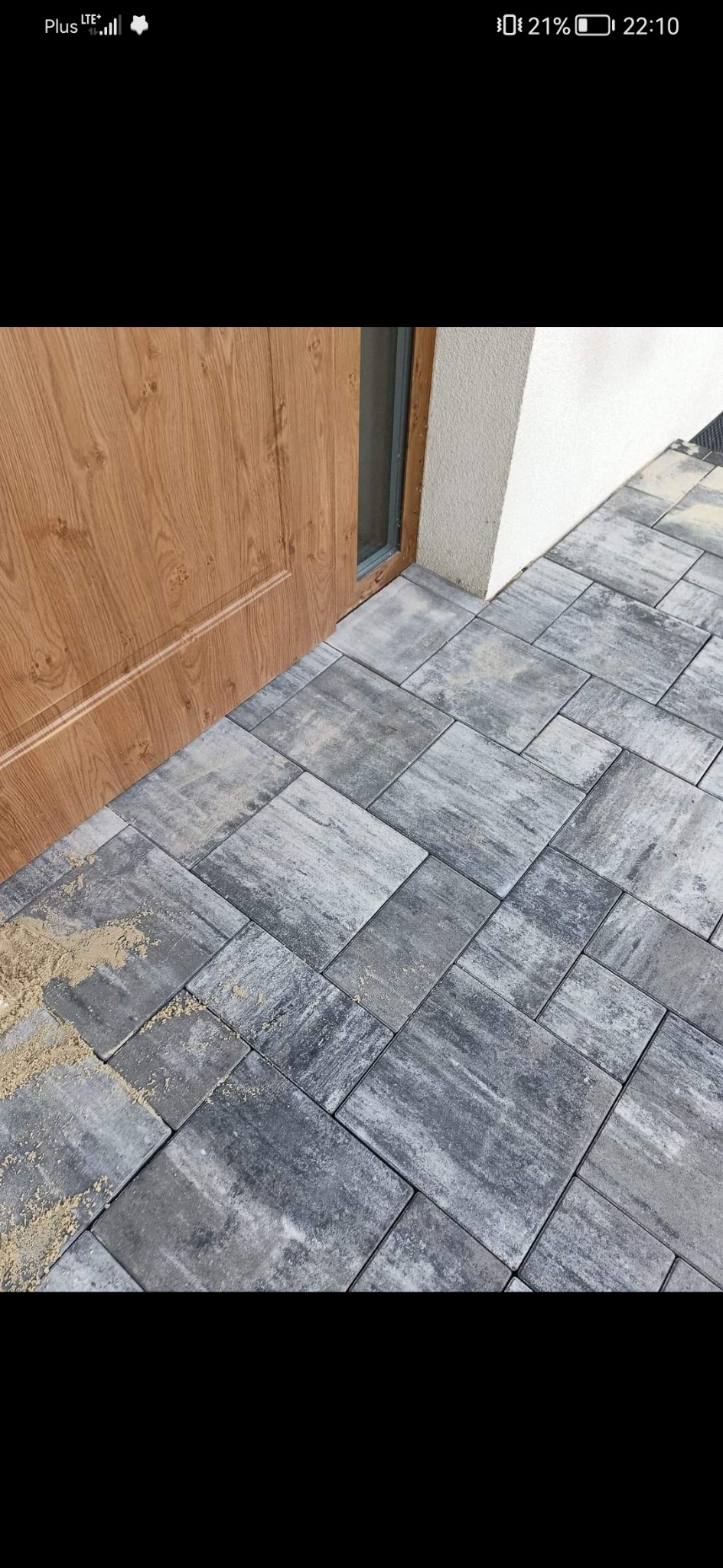 Ułożona szara kostka brukowa przy wejściu do domu, widoczne resztki piasku fugowego.