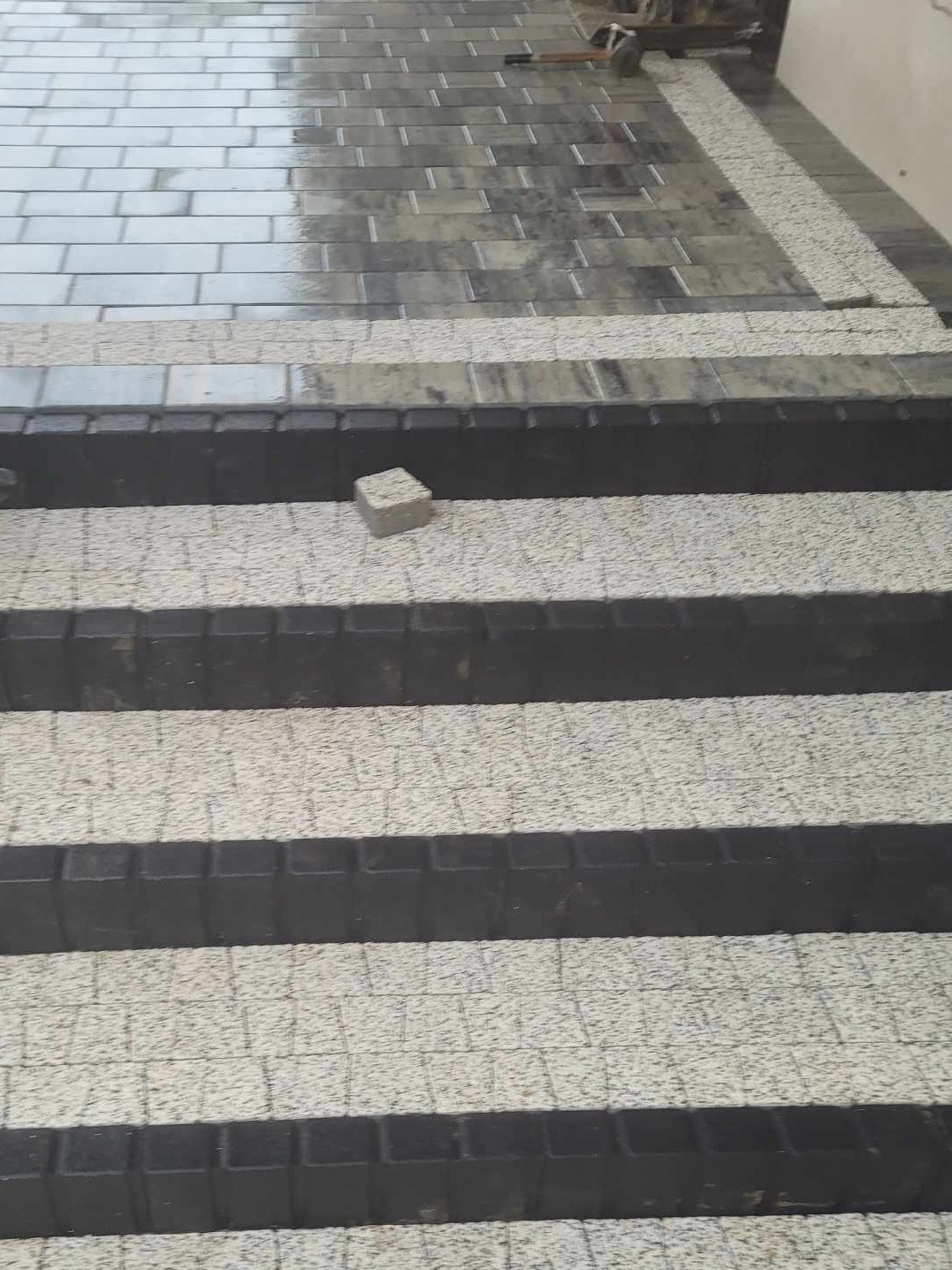 Schody zewnętrzne wyłożone kostką granitową w dwóch odcieniach szarości, z pojedynczą kostką leżącą na drugim stopniu od góry.