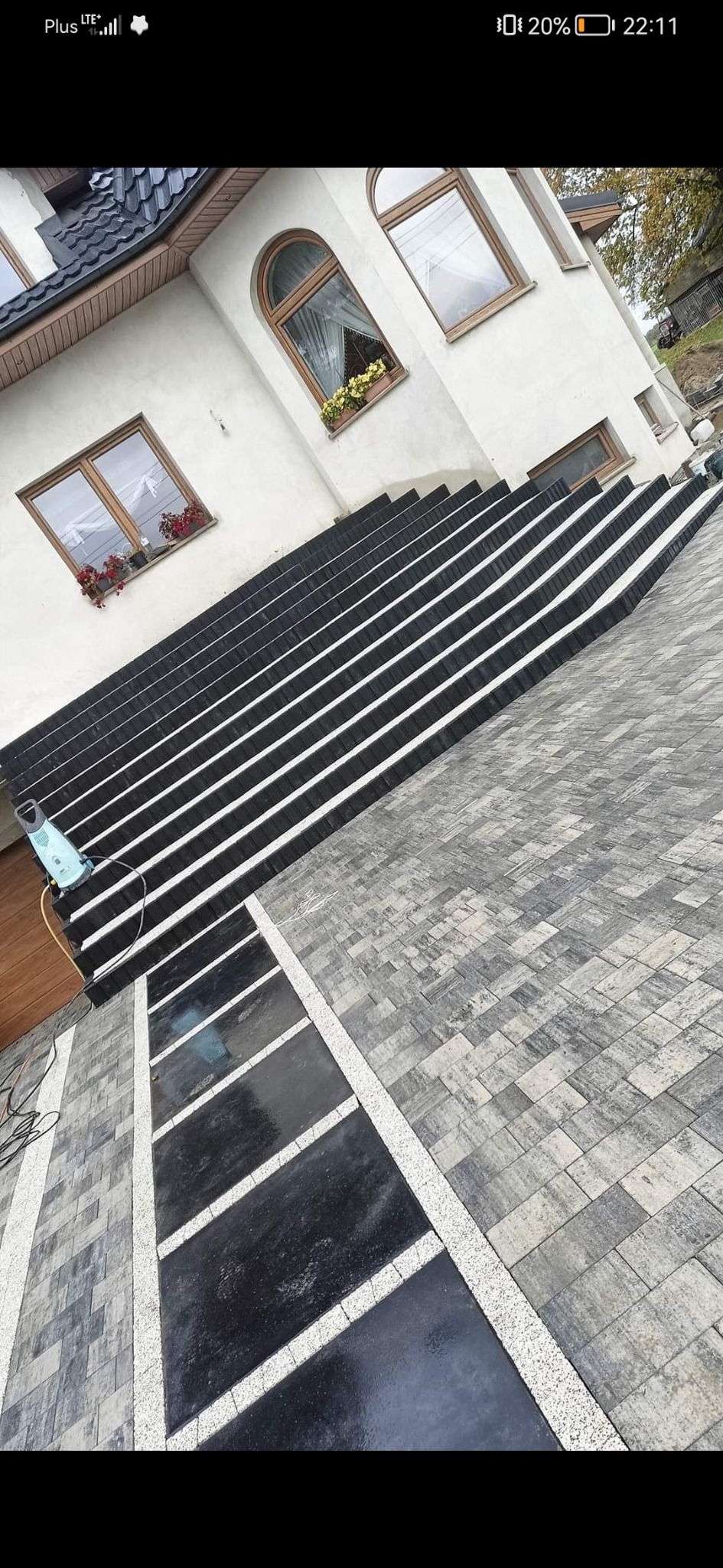 Ułożona kostka brukowa w Głownie: Schody wejściowe z czarnej kostki brukowej z białymi fugami, przechodzące w szarą kostkę na podjeździe, widok z góry.