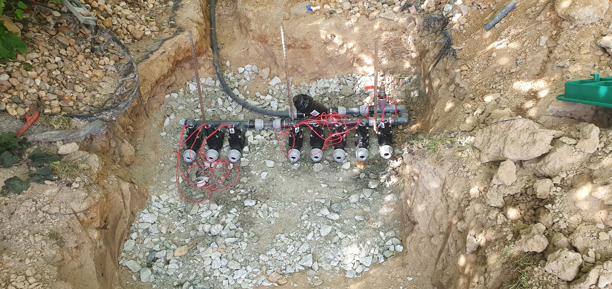 Wykonany wykop z instalacją nawadniającą z elektrozaworami, widoczne przewody i kamieniste podłoże.