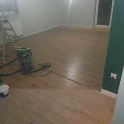 Konrad - Pokój po ułożeniu paneli podłogowych, widoczny odkurzacz przemysłowy, drabina malarska i częściowo pomalowana ściana na zielono.