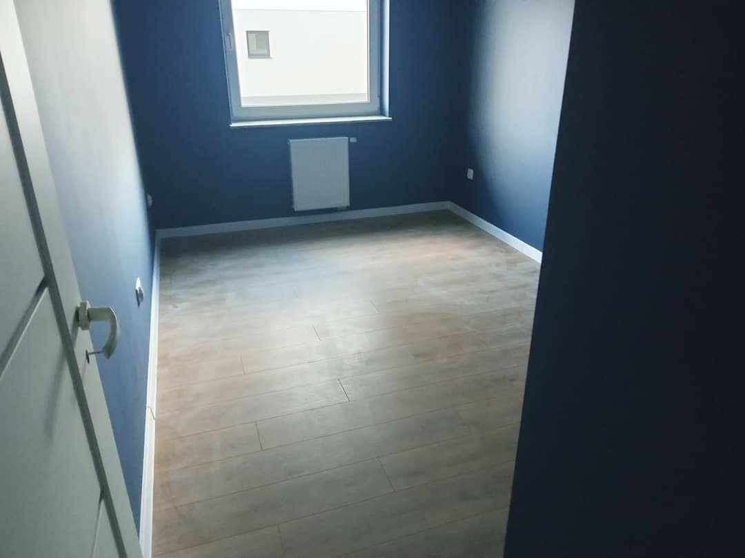 Pusty pokój z nowymi panelami podłogowymi, świeżo pomalowanymi ścianami w kolorze granatowym i białym grzejnikiem pod oknem.