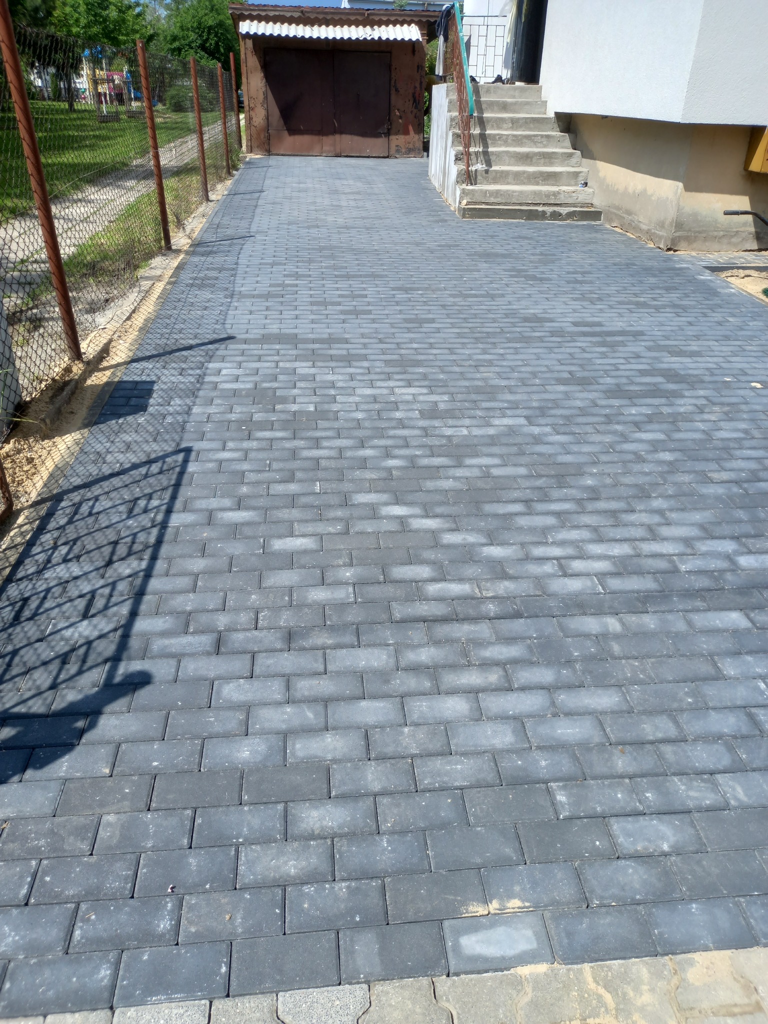 Ułożona szara kostka brukowa prowadząca do garażu i schodów wejściowych, widoczny cień ogrodzenia.