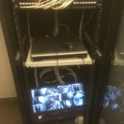 Szafa rack z zamontowanym switchem PoE Alhua, rejestratorem Hikvision z podłączoną myszą i monitorem Hikvision wyświetlającym podgląd z kamer monitoringu.