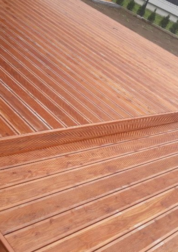Ukośnie ułożone deski tarasowe z drewna egzotycznego, tworzące dwupoziomowy taras z widocznym ogrodzeniem w tle.