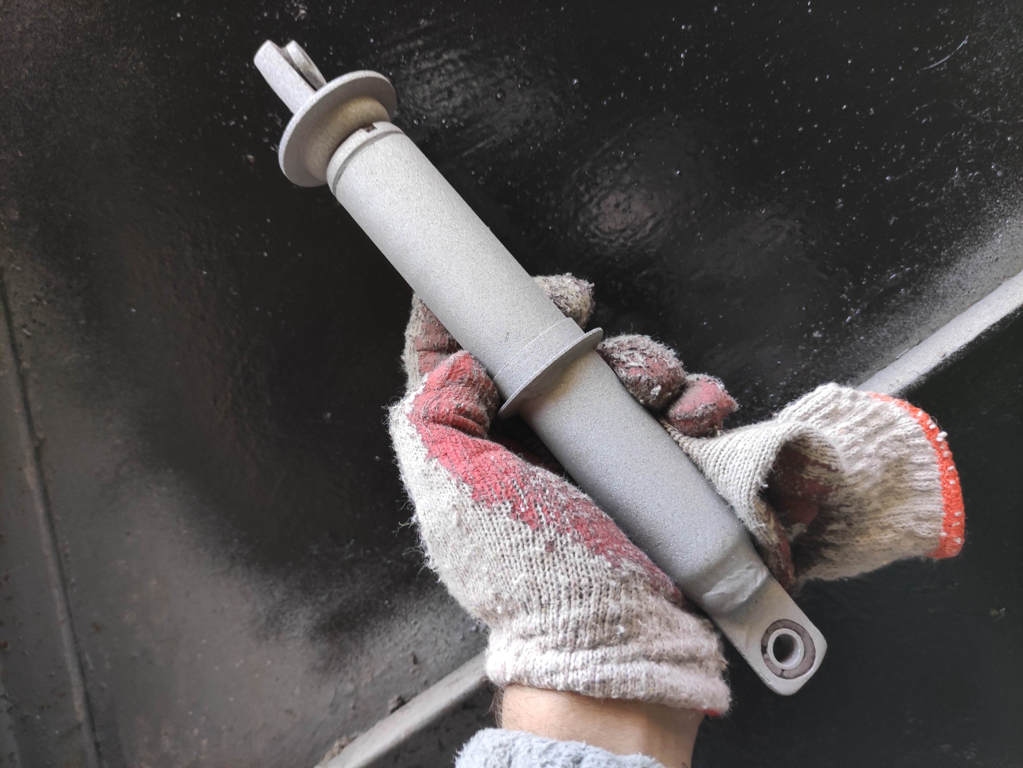 Szlifowany, metalowy element konstrukcyjny w rękawicy roboczej na tle ciemnej powierzchni, prawdopodobnie element spawany lub odlewany.