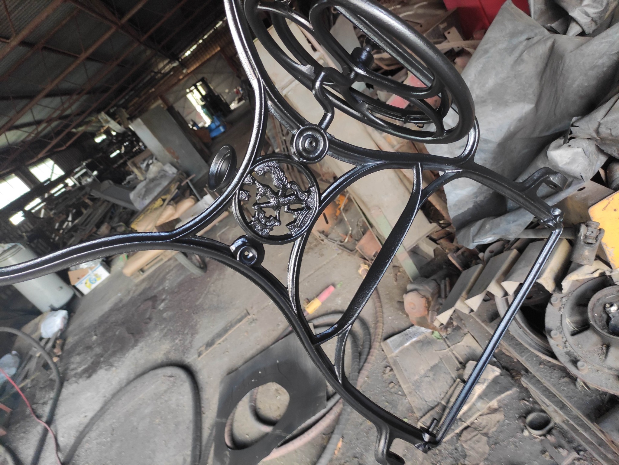 Fragment czarnej, metalowej konstrukcji z dekoracyjnym ornamentem w kształcie gryfa, prawdopodobnie element balustrady lub poręczy, sfotografowany w warsztacie.