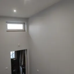 Wnętrze domu po malowaniu ścian na szaro, widoczny fragment schodów, okno pod sufitem i oświetlenie punktowe