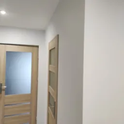 Dwa drewniane drzwi wewnętrzne z przeszkleniami, pomalowane ściany na szaro, widok z perspektywy niskiego kąta.