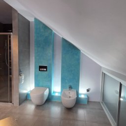 Krzysztof Bączyński - Nowoczesna łazienka na poddaszu z toaletą, bidetem i kabiną prysznicową. Ściany zdobią turkusowe pasy z podświetleniem LED. Szare płytki podłogowe i biały sufit.