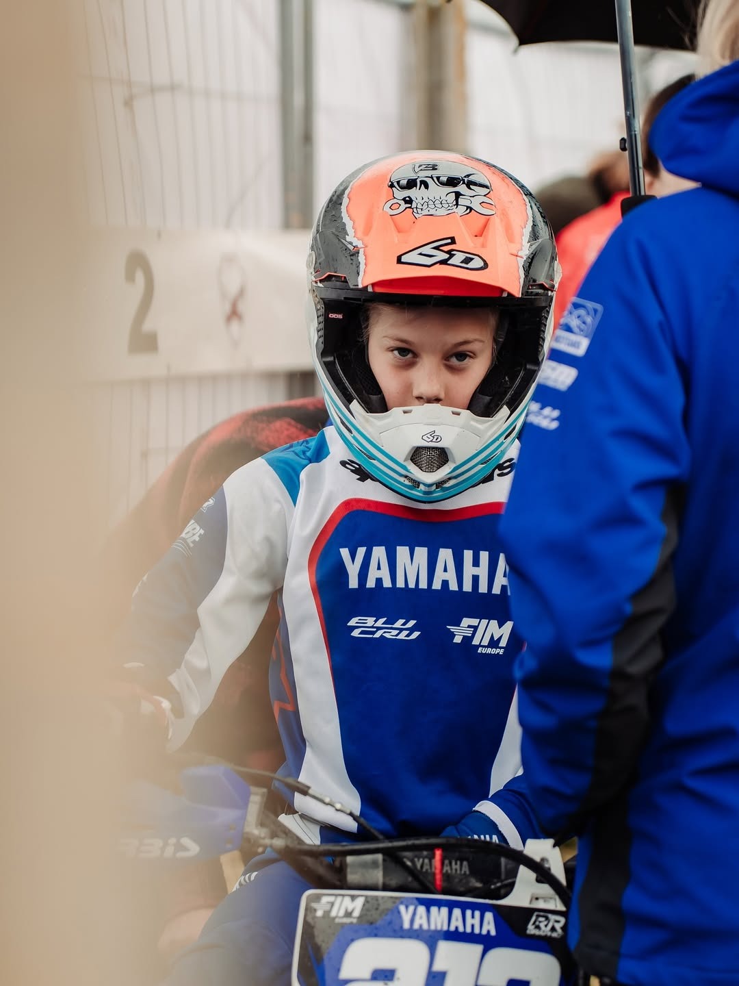 Młody motocyklista w kasku z motywem czaszki, w stroju Yamaha, czeka na start zawodów motocrossowych. Ujęcie z bliska, skupione na twarzy zawodnika.