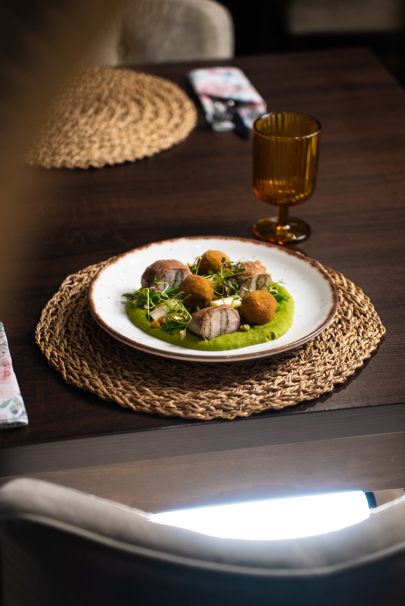 Apetyczne danie na talerzu z dekoracyjną podkładką, obok szklanka na ciemnym drewnianym stole. Stonowana kolorystyka i naturalne światło podkreślają kulinarną kompozycję.