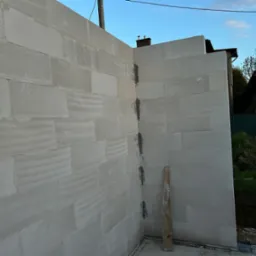 Wznoszenie ścian z bloczków betonu komórkowego Ytong na fundamencie, widoczny fragment narożnika z zaprawą i drewniana listwa oparta o ścianę.