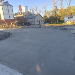 PPSW - Świeżo wylana, gładka betonowa nawierzchnia placu manewrowego w gospodarstwie rolnym, z widocznymi szalunkami i zbrojeniem na obrzeżach, w tle budynki gospodarcze i silosy.