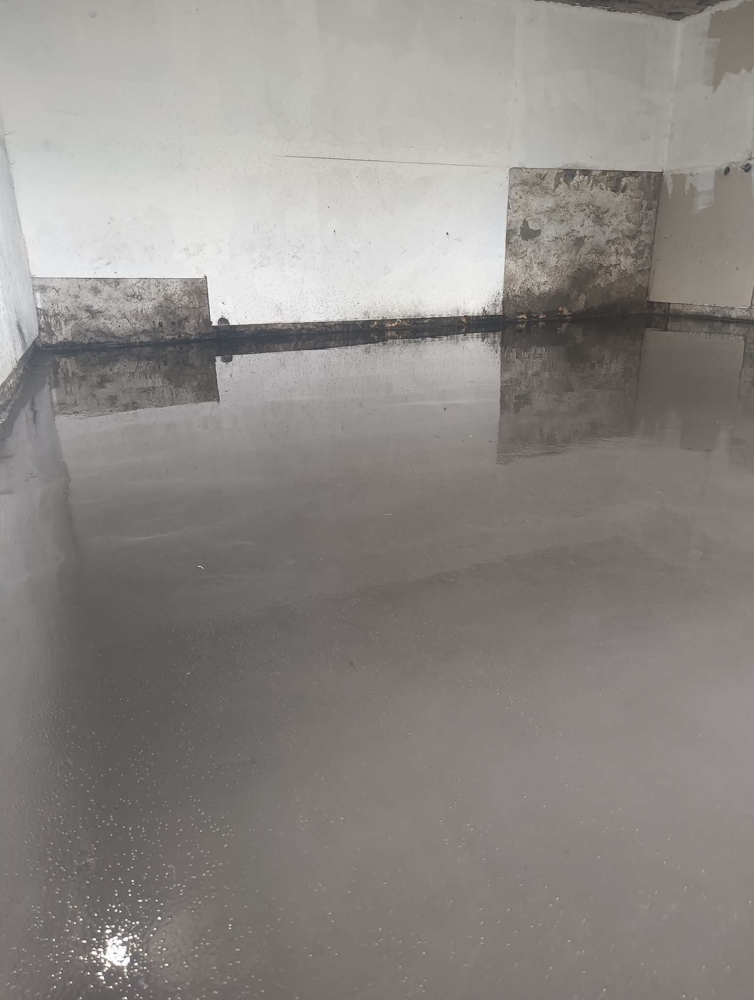 Świeżo wylana, samopoziomująca szara wylewka na podłodze w surowym pomieszczeniu z częściowo wykończonymi ścianami.