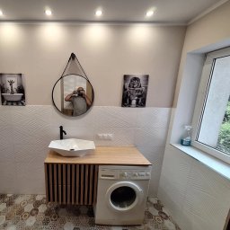 M-BUD YEVHENII MULIAR - Nowoczesna łazienka z umywalką nablatową, szafką z lamelami, pralką i dekoracyjnymi obrazami na ścianie. W lustrze odbija się osoba robiąca zdjęcie.