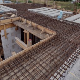 Centra - Zbrojenie stropu na budowie domu murowanego, widoczne szalunki, betonowe bloczki i siatka z prętów zbrojeniowych.