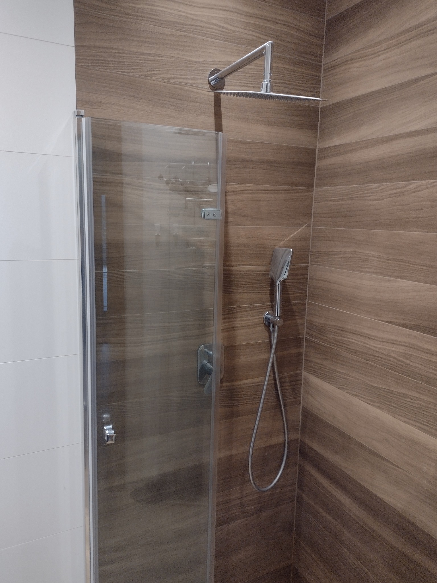 Kabina prysznicowa z deszczownicą i słuchawką, wykończona płytkami imitującymi drewno w ciepłych odcieniach brązu.