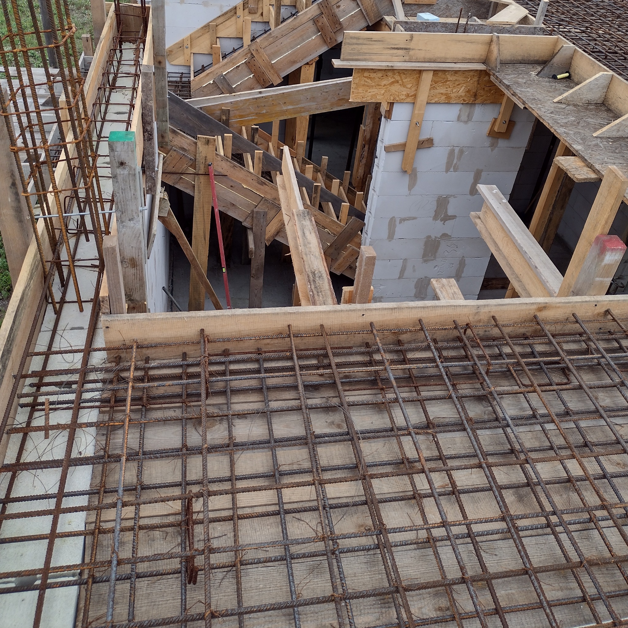 Zbrojenie płyty fundamentowej z deskowaniem i częściowo wymurowanymi ścianami z betonu komórkowego w tle.