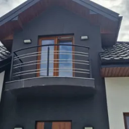 Elewacja domu w Spiczynie z balkonem i nowoczesną, metalową balustradą z poziomych prętów, widok z dołu.