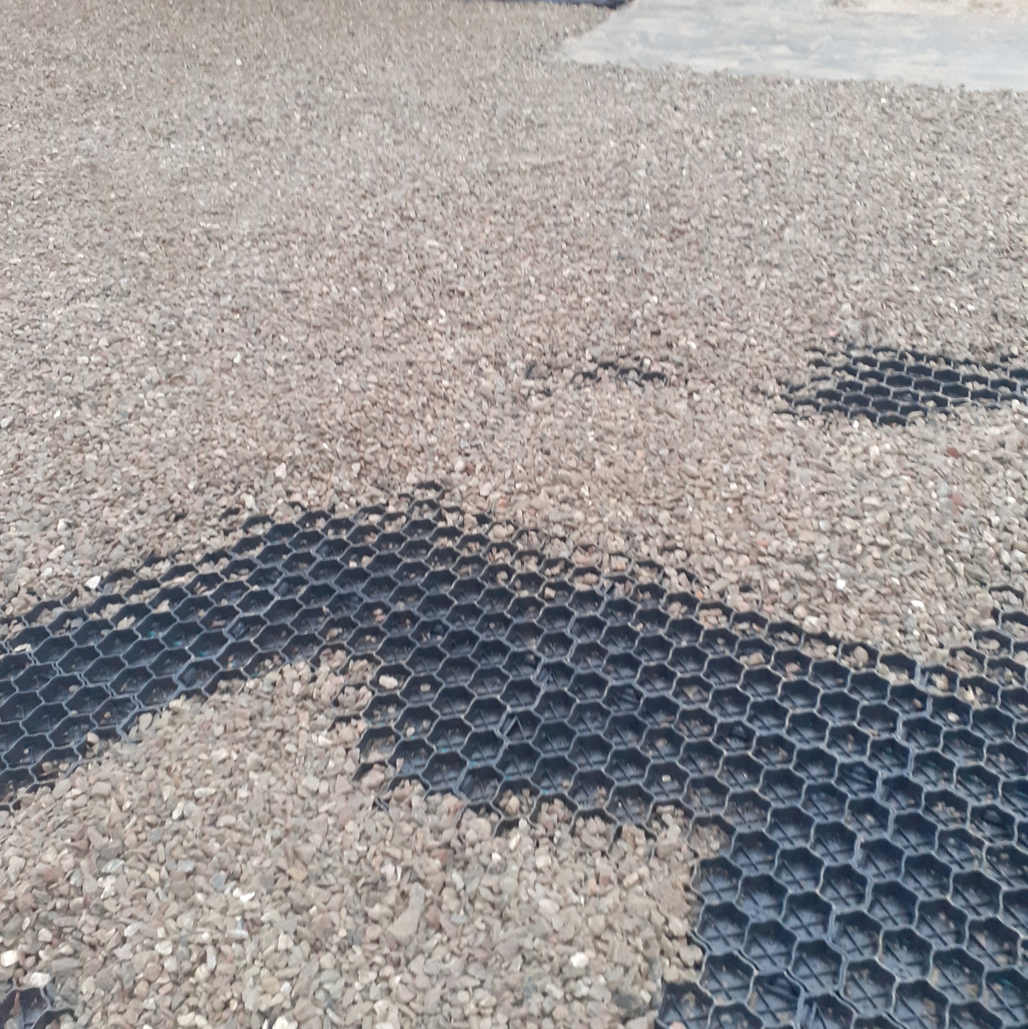 Częściowo wypełniona kruszywem geokrata na powierzchni gruntu, widok z góry.