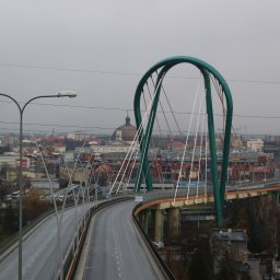 Biuro Usług Geodezyjnych DELTA - Most wantowy z zielonym łukiem w Grudziądzu, widok na miasto w pochmurny dzień, przewody elektryczne przecinają kadr.