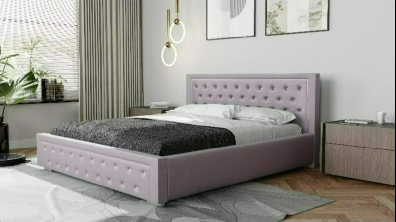 Łóżko tapicerowane w odcieniach fioletu z pikowanym zagłówkiem, pościelone białą pościelą i szarym pledem, ustawione w sypialni z drewnianymi szafkami nocnymi i lampami wiszącymi.