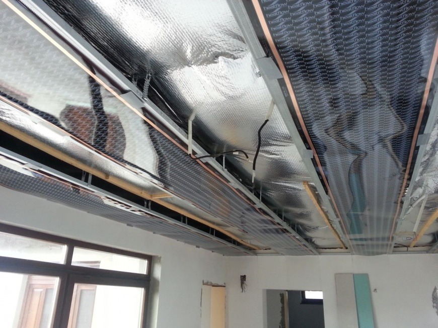 Montaż sufitowego systemu grzewczego z widocznymi matami grzewczymi, folią aluminiową i elementami konstrukcyjnymi w trakcie instalacji w nowym budynku.