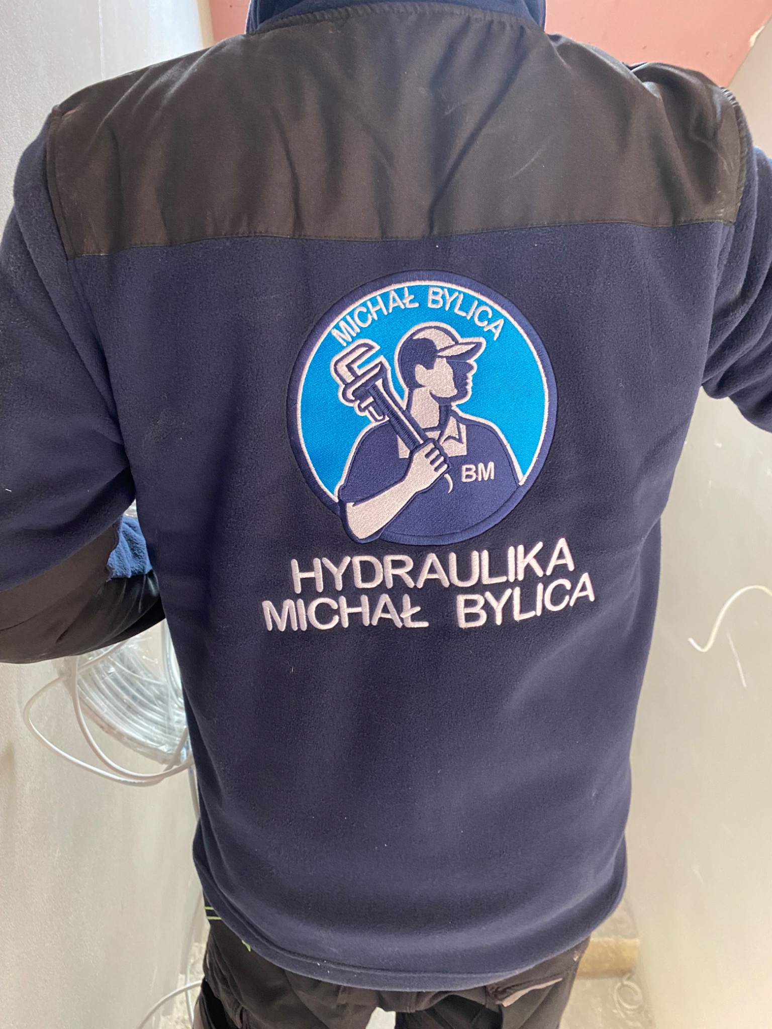 Bluza robocza hydraulika z Trzebuni z naszytym logo firmy: sylwetka hydraulika z kluczem francuskim na tle koła oraz napisem 'Hydraulika Michał Bylica'.