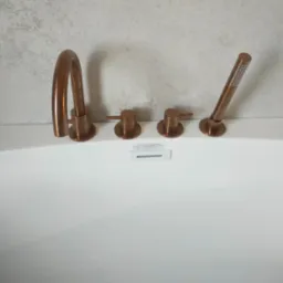 Miedziana bateria wannowa marki Scandibath na tle białej wanny i jasnej ściany o fakturze betonu. Minimalistyczny design.