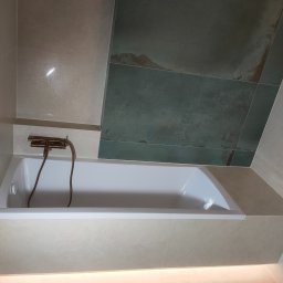 Patryk Furlepa Budownictwo remontowo wykończeniowe - Nowoczesna łazienka z wanną, beżowymi płytkami i akcentem zieleni na ścianie. Miedziana armatura dodaje elegancji. Podświetlenie LED podkreśla minimalistyczny design.