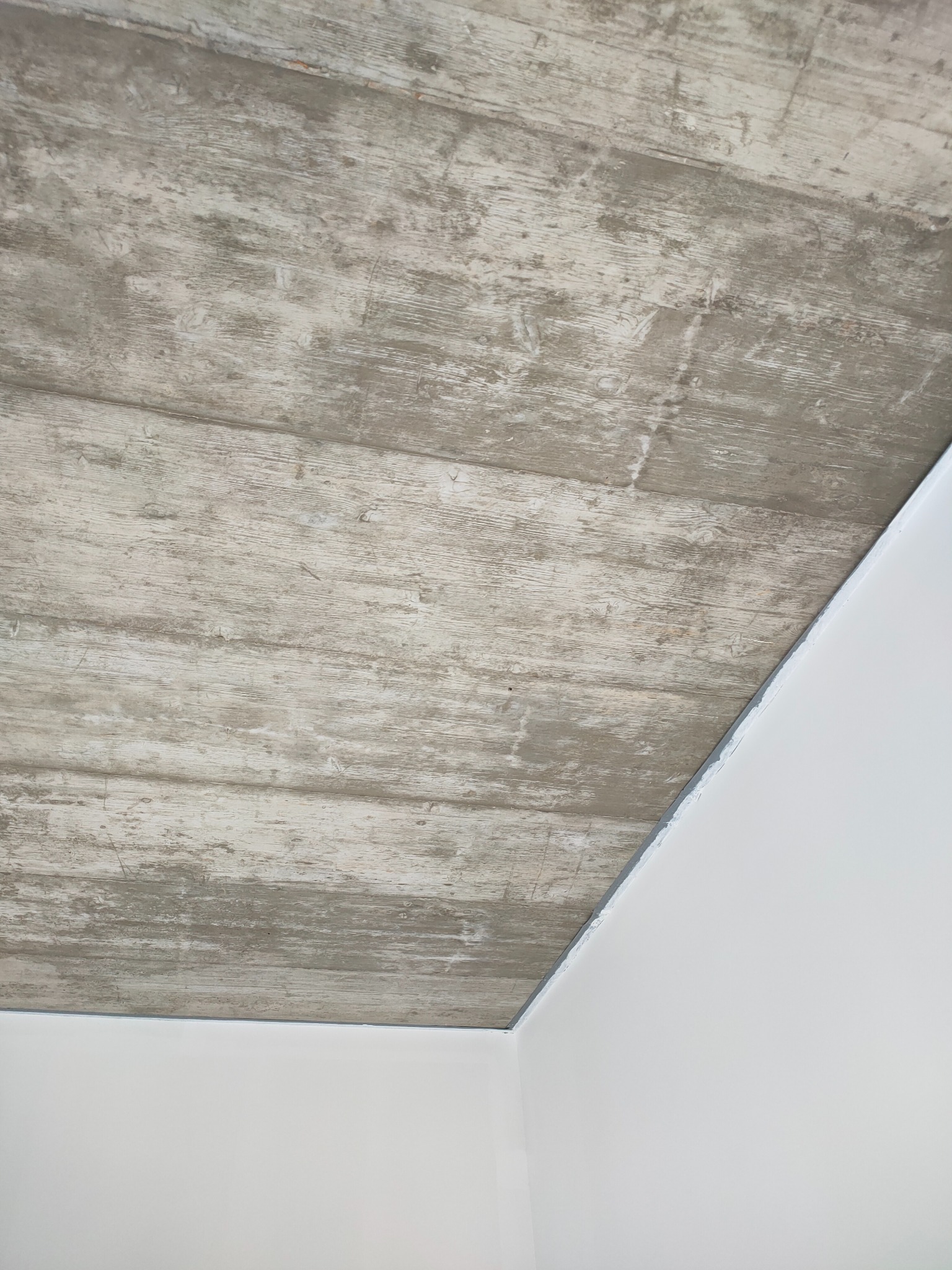 Wykończony sufit z efektem betonu architektonicznego, widoczny narożnik pomieszczenia z białymi ścianami. Realizacja wykończenia wnętrza z bliska.