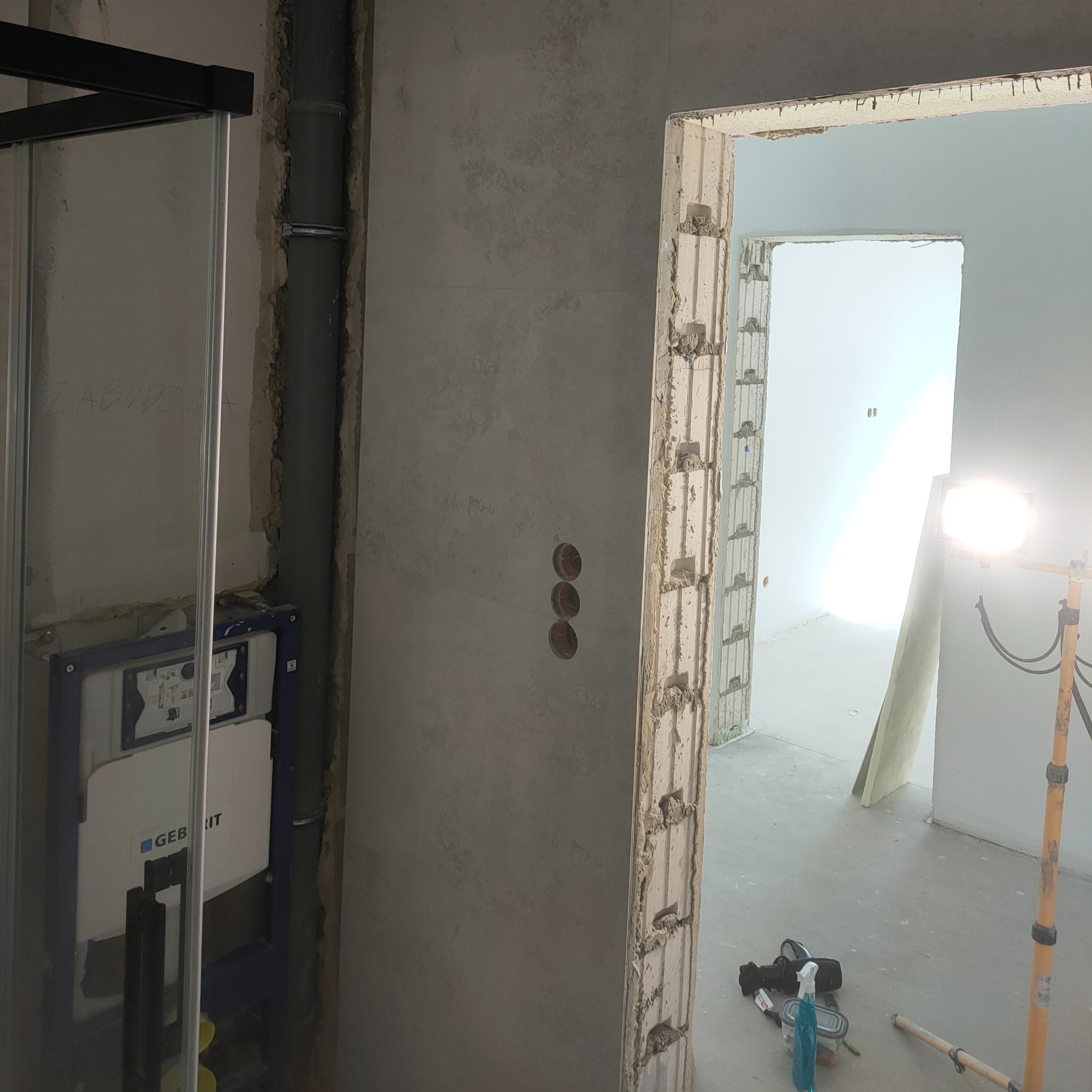Łazienka w trakcie remontu: widoczna zabudowa stelaża WC Geberit, surowa ściana z przygotowanymi otworami pod gniazdka oraz fragment kabiny prysznicowej.