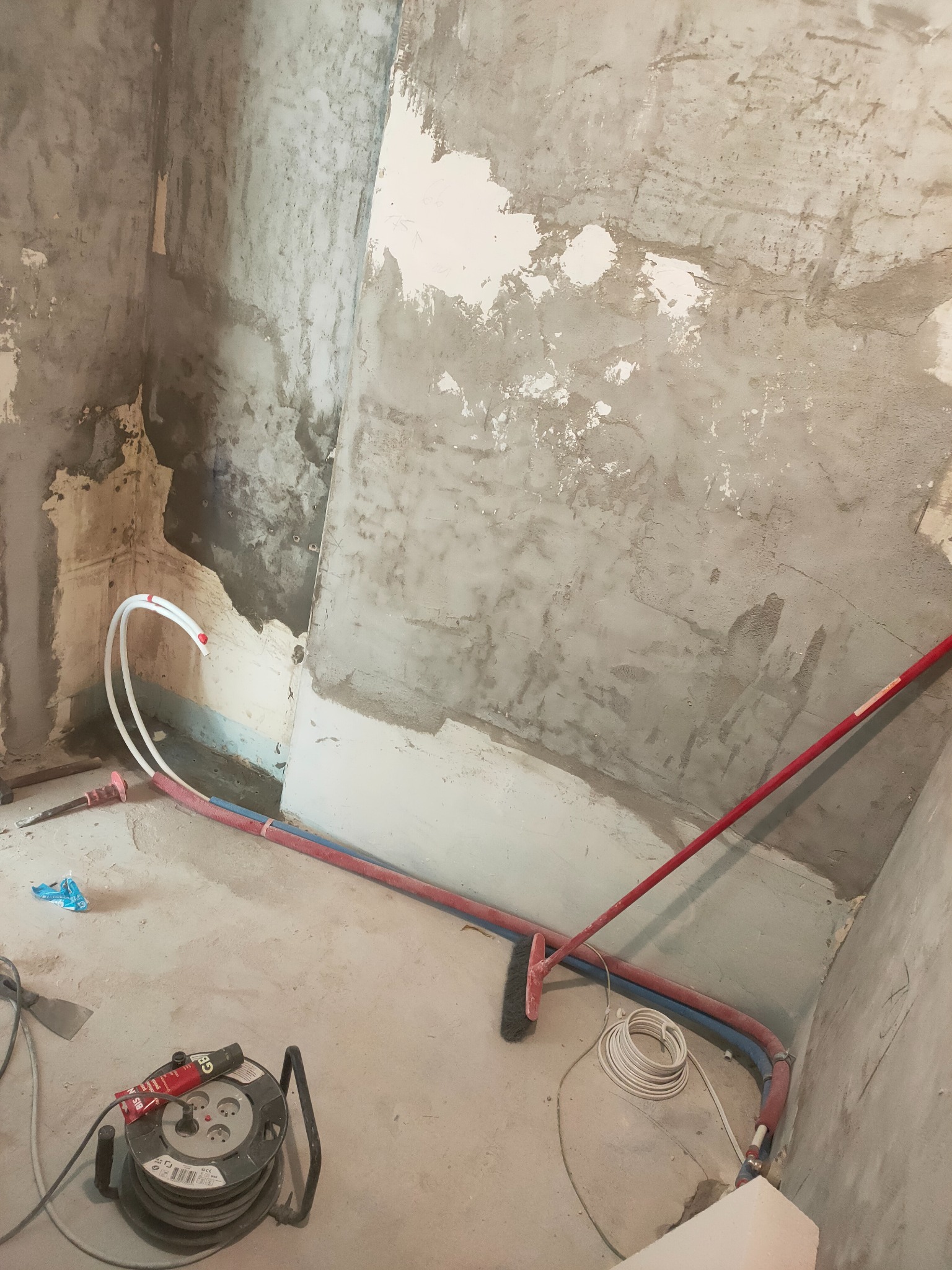 Surowy stan łazienki w trakcie remontu: ściany z resztkami starej farby, widoczne rury instalacji wodnej i elektrycznej, przed położeniem płytek.