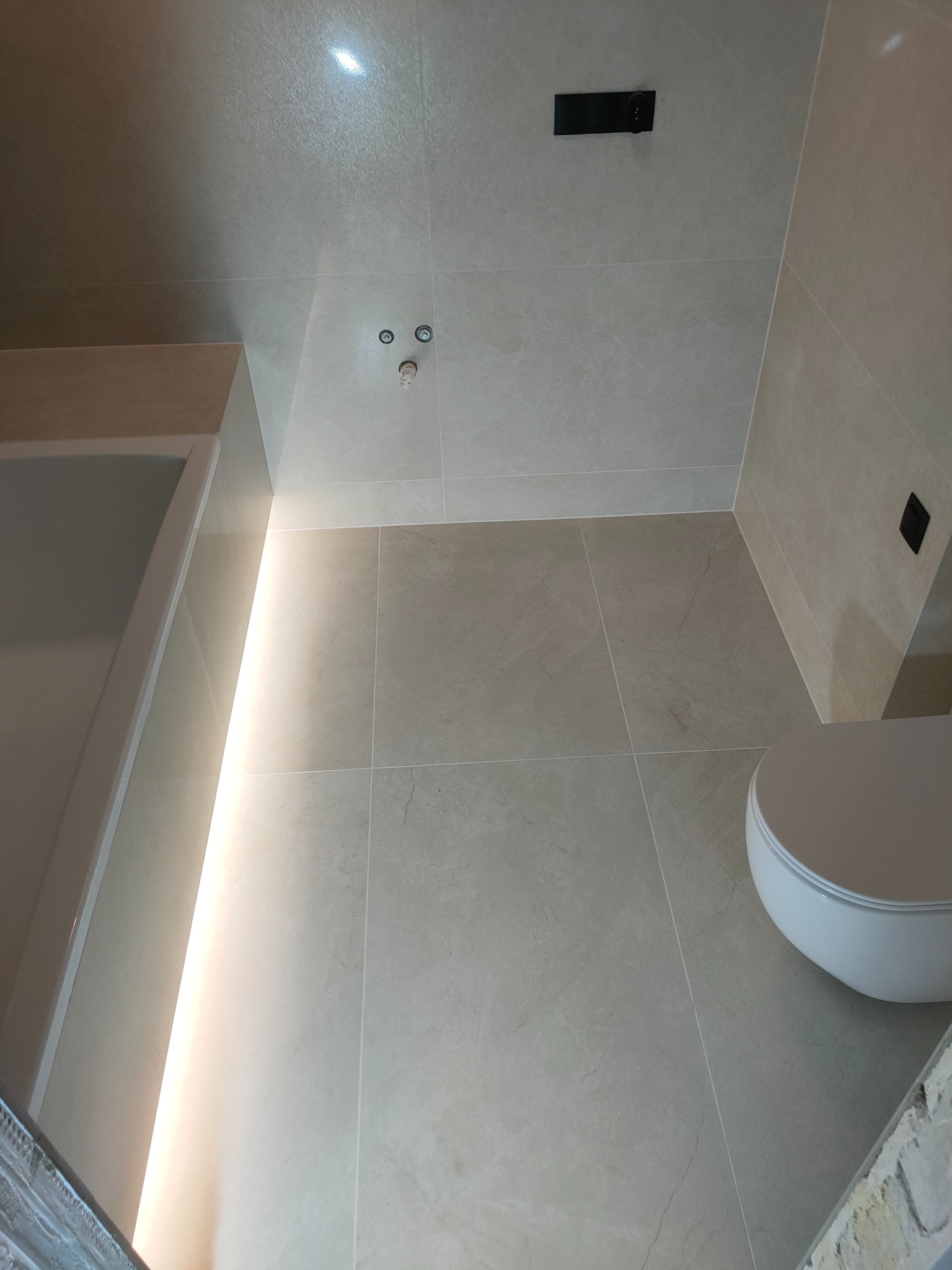 Beżowa łazienka po remoncie: płytki na ścianach i podłodze, podświetlona wanna, toaleta. Widok z góry podkreśla minimalistyczny design i precyzję wykonania.