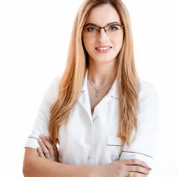 Portret uśmiechniętej blondynki w okularach i białym uniformie medycznym z rękami skrzyżowanymi na białym tle.