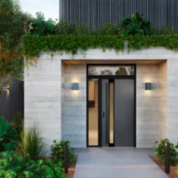 Nowoczesne drzwi zewnętrzne w minimalistycznym betonowym otoczeniu z zielenią, oświetlone lampami ściennymi, z widocznym fragmentem przeszklenia i czarną ramą.