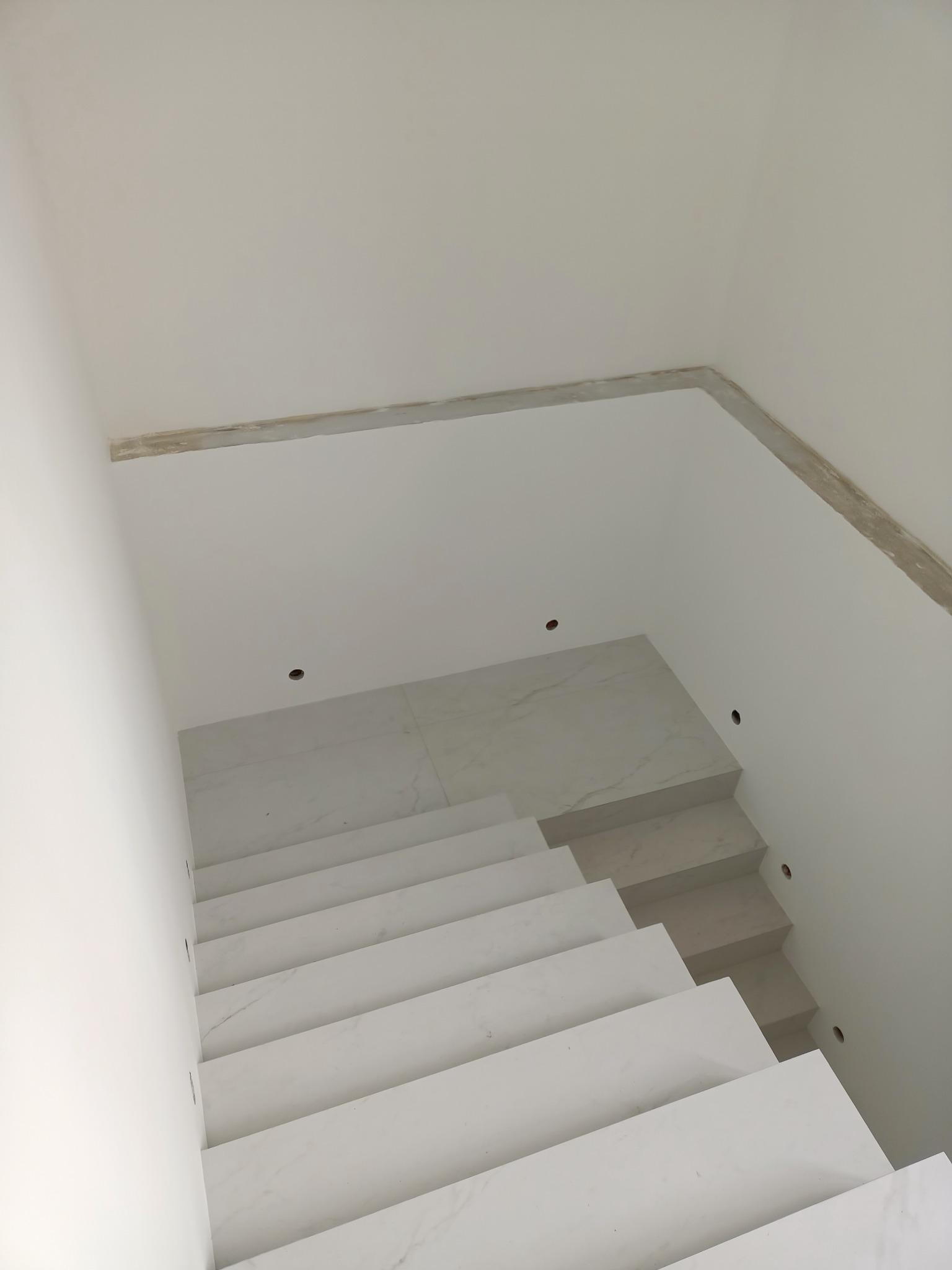 Wykończone schody wewnętrzne z białego marmuru, prowadzące w dół, widok z góry, z widocznymi otworami na oświetlenie w ścianie.
