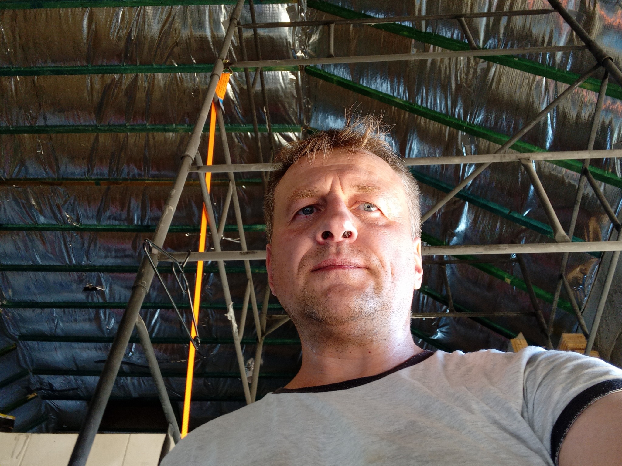 Mężczyzna spogląda w górę na metalową konstrukcję z folią izolacyjną i pomarańczowymi pasami mocującymi.