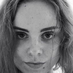 Henryk Szymański Fotografia - Czarno-biały portret kobiety z bliska, z widocznymi piegami i rozpuszczonymi włosami, skierowana prosto w obiektyw, z intensywnym spojrzeniem.