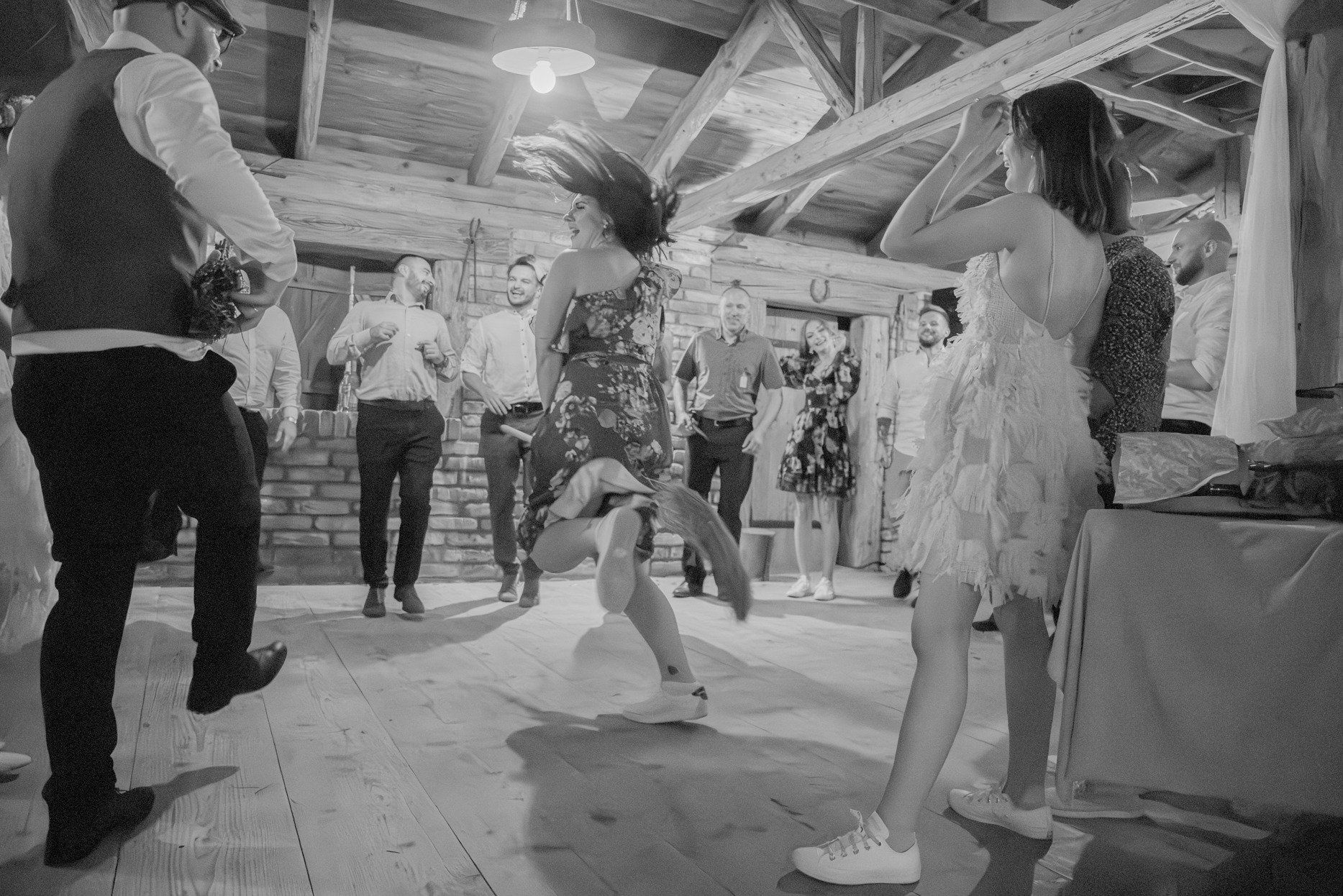 Radosne tańce weselne w Rzeszowie: czarno-białe ujęcie z parkietu, gdzie panna młoda wiruje w sukience w kwiaty, a goście świętują w tle.