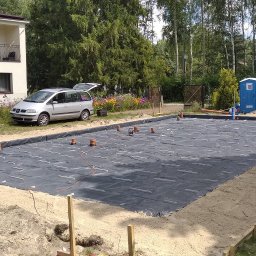 DOM PROJEKT STABILNY FUNDAMENT sp. z o.o - Przygotowany teren pod budowę z rozłożoną folią izolacyjną, wystającymi rurami wentylacyjnymi i widocznym szarym samochodem osobowym w tle.