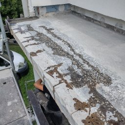 Jakub Łukomski - Przygotowanie balkonu do remontu: widoczne ślady po demontażu starej warstwy, odsłonięty beton z widocznymi kamykami, fragment rusztowania i pracownik w odzieży roboczej.