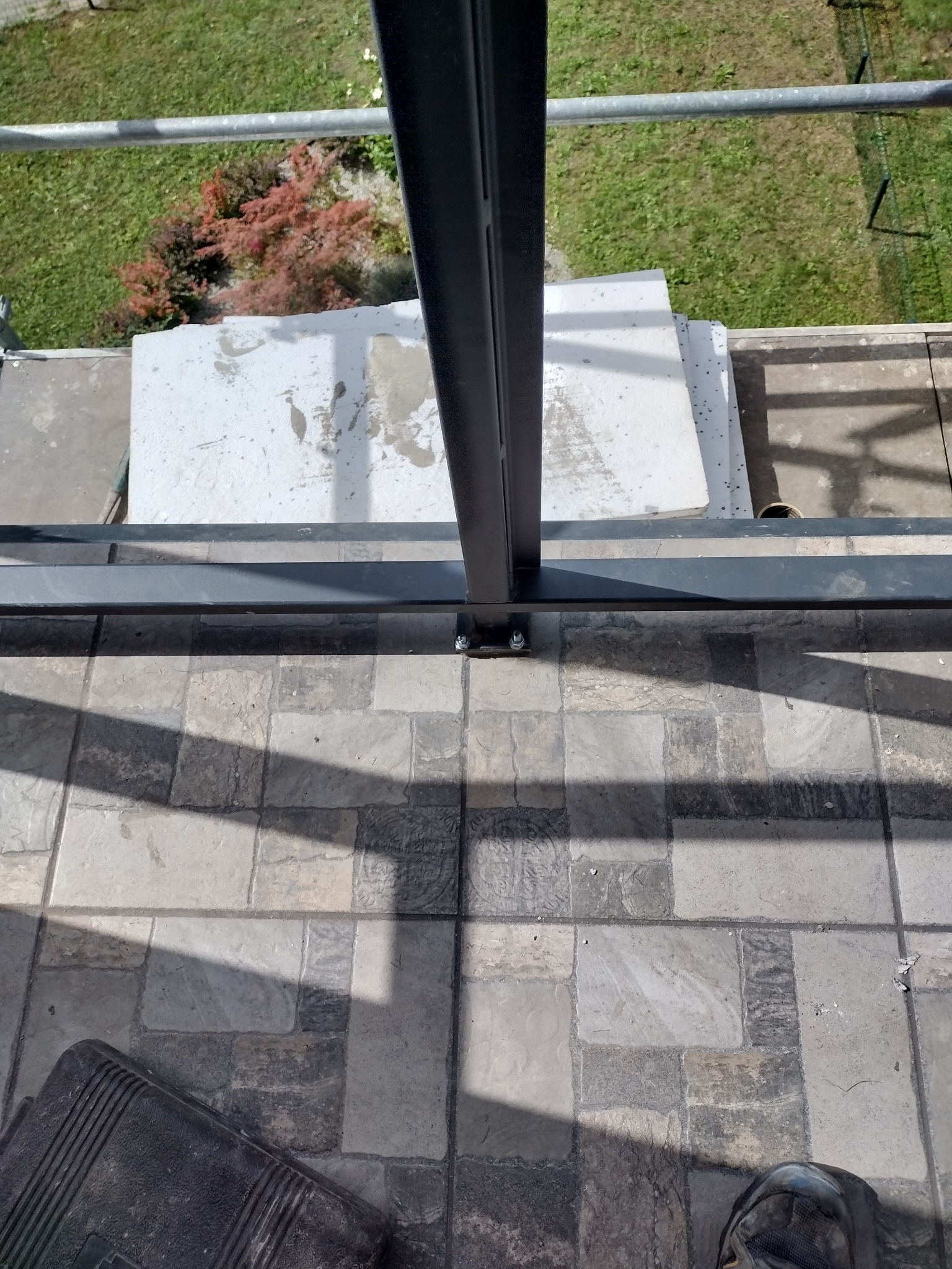 Widok z góry na fragment balkonu z nową, szarą, wzorzystą terakotą, elementami metalowej konstrukcji i fragmentem narzędzi w rogu.