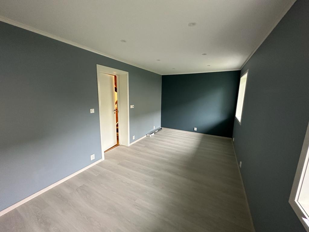 Pomalowane na szaro wnętrze pokoju z panelami podłogowymi, białą stolarką drzwiową i listwami przypodłogowymi.