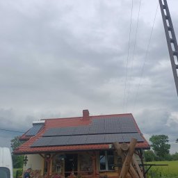 DanLuk Daniel Łukaszewski - Dom jednorodzinny z panelami słonecznymi na dachu, dodatkowo kolektory słoneczne, widok z poziomu gruntu w pochmurny dzień.