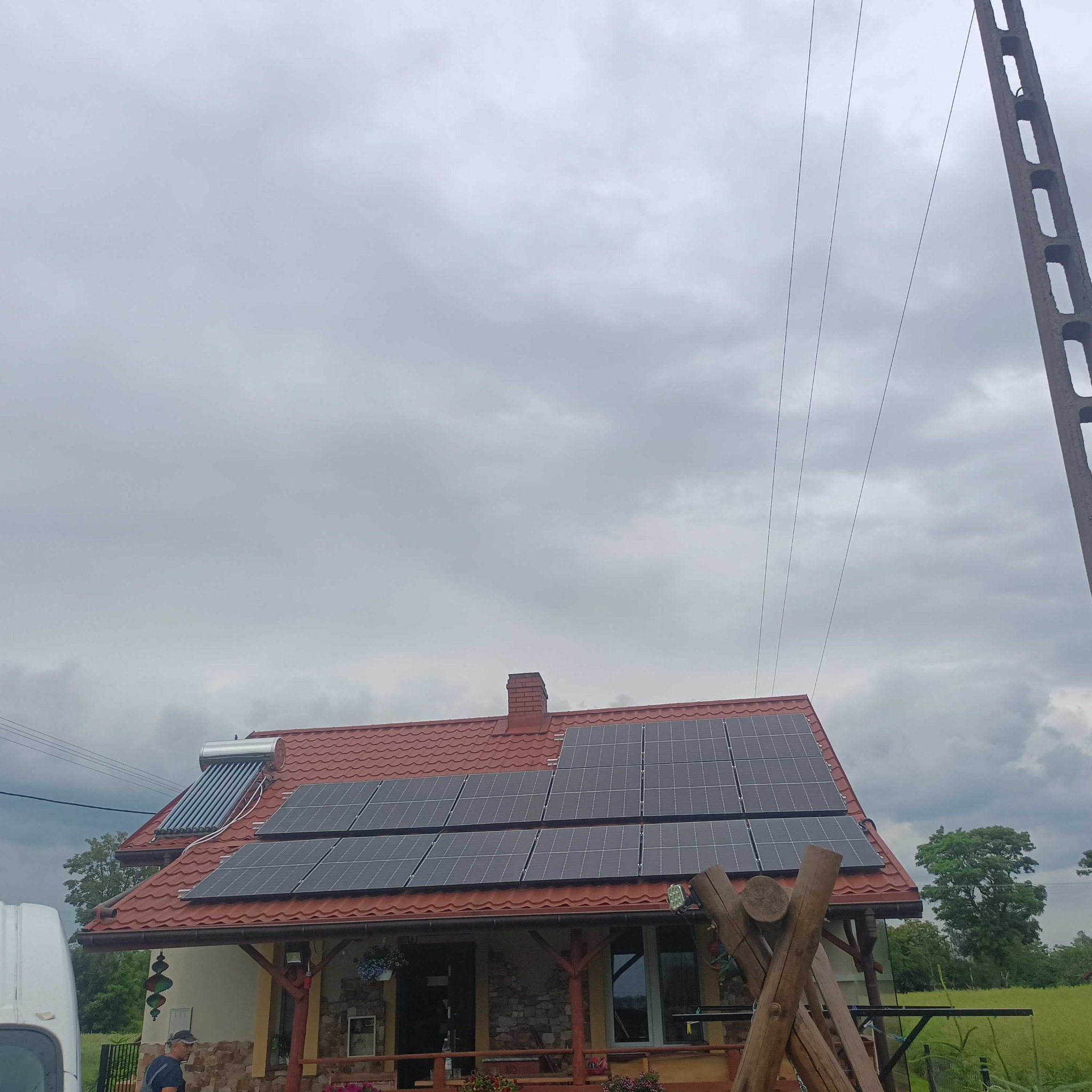 Dom jednorodzinny z panelami słonecznymi na dachu, dodatkowo kolektory słoneczne, widok z poziomu gruntu w pochmurny dzień.