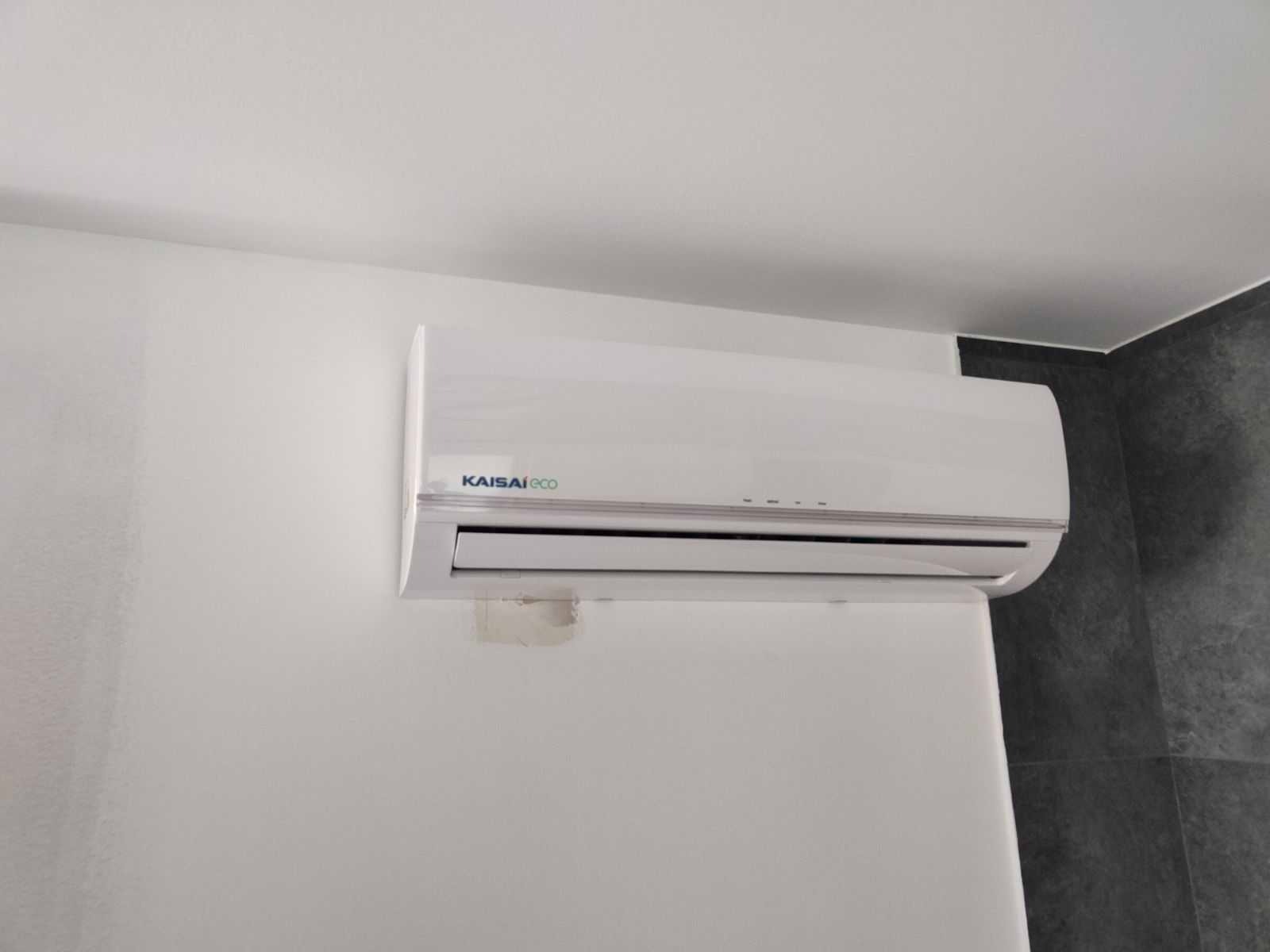 Biała jednostka wewnętrzna klimatyzacji Kaisai Eco zamontowana na ścianie, widoczne ślady po taśmie montażowej.